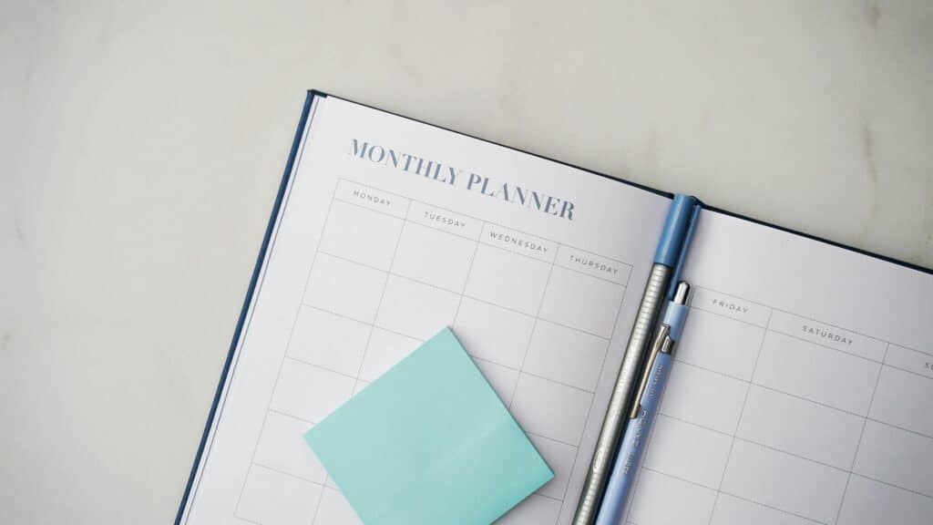 Empty planner, open at a month with pens and a post it note pad showing that something needs to be planned